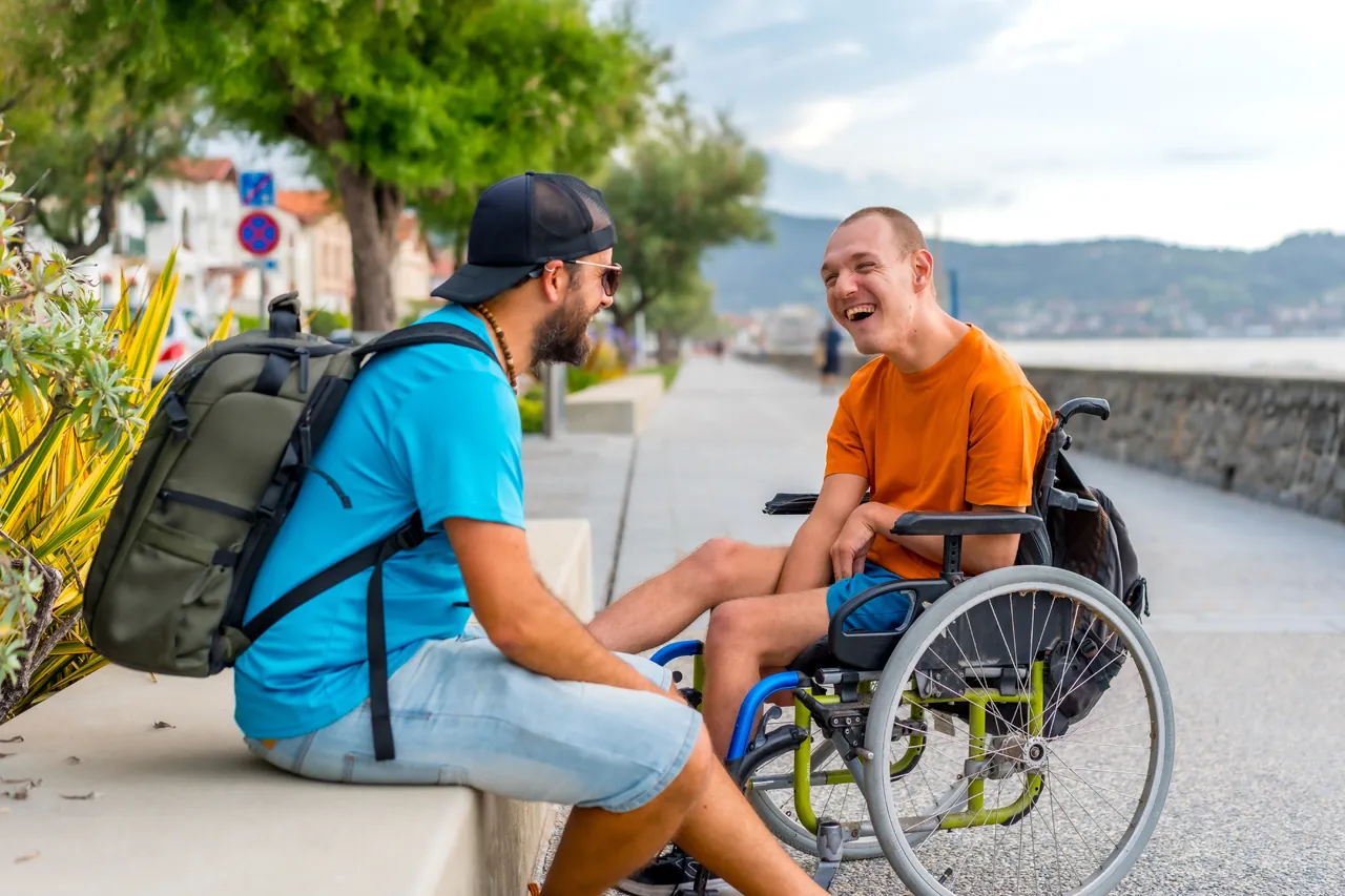 Two friends talking outdoors, one using a wheelchair